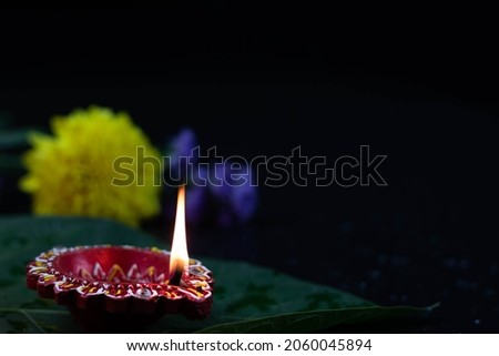 Closeup Of Eco Friendly Handcrafted Red Clay Diya Deep Or Dia Illuminated On Green Leaf With Flowers. Indian Festival Theme For Diwali Pooja, Navratri, Dussehra Puja, Deepawali Or Shubh Deepavali