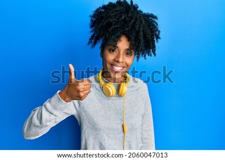 African american woman with afro hair wearing sweatshirt and using headphones smiling happy and positive, thumb up doing excellent and approval sign 