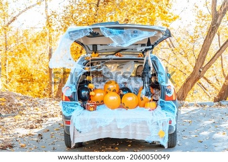 cute trunk of car decorated for Halloween with cobwebs, orange balloons, pumpkins and sweets, the outdoor creative activity concept in autumn in October