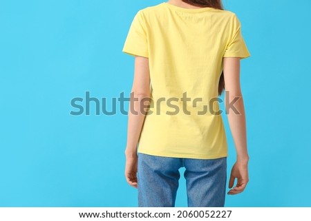 Young woman in modern t-shirt on color background, back view