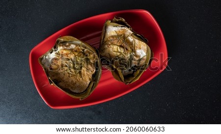 Top view steamed curry fish in banana leaf cups or Thailand name Hor Mok Pla. is placed on a red plate in the center of the picture. and placed on the black tiled floor.