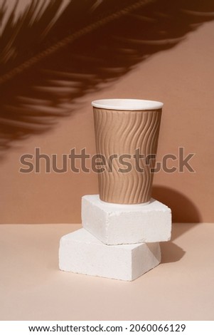 Podium made of natural stone with the shadow of tropical leaves in the background, paper cups. Beautiful background from natural materials