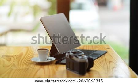 Side view, Modern tablet computer stand on wooden table with camera and coffee cup over blurred background.