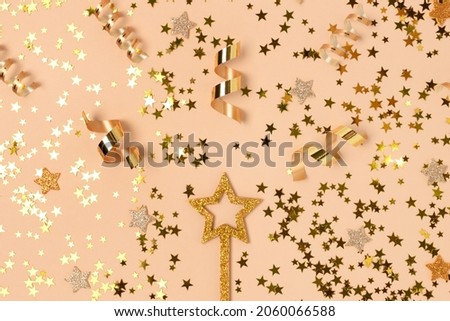 Glittering magic wand with gold colored confetti on a beige background.