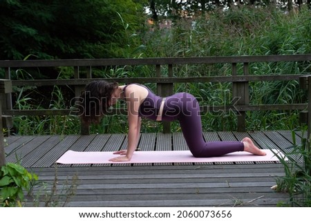 A young sporty healthy woman doing the cow pose during her yoga session. She is wearing a purple yoga clothing set. A pose that is good for your back and health. 
