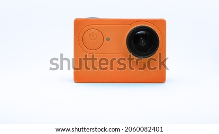High-resolution orange action camera from the side of the power button and the lens built into it against a light background