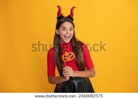 glad teen girl wearing imp horns holding pumpkin party accessory, happy halloween.