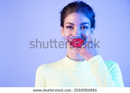 Funny girl with full fake  lips on neon background. Woman with the painted red lips on her hand.  Emotion of joy and positive. Concept of fun and tomfoolery.