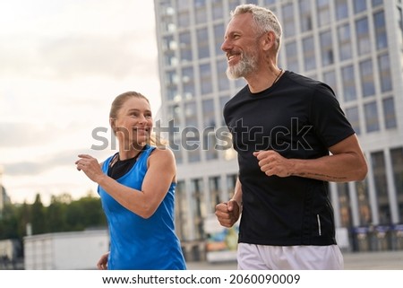 Portrait of active middle aged couple, man and woman in sportswear looking happy while jogging together outdoors, having mroning workout Royalty-Free Stock Photo #2060090009