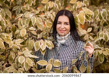 A young girl in a white sweater and plaid coat in an autumn park surrounded by foliage