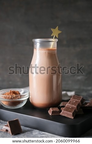 Tray with bottle of aromatic chocolate milk on dark background
