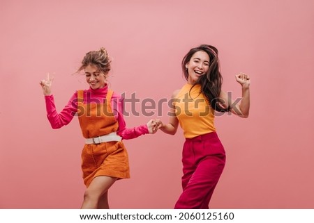 Bright young females of different nationalities dance and jump holding hands with copy space. Professional shot of two best friends having fun and laughing out loud. Leisure and lifestyle concept Royalty-Free Stock Photo #2060125160