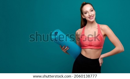 Young sporty smiling woman in sportswear holding yoga mat in her hands