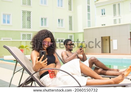 young african friends chilling near a pool, using their phones