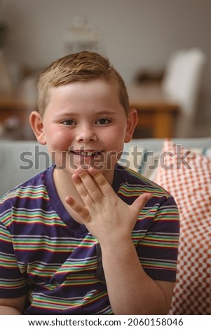 Portrait of caucasian boy making hand gestures sitting on the couch at home. sign language learning concept