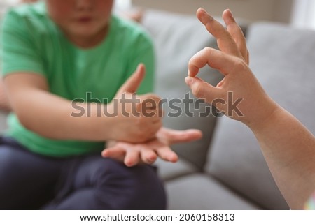 Two caucasian boys communicating using sign language while sitting on the couch at home. sign language learning concept