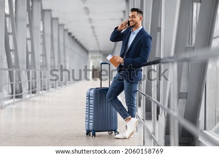 Mobile Call. Smiling Young Middle Eastern Businessman Talking On Cellphone In Airport While Waiting With Suitcase For Flight At Terminal, Happy Arab Man Having Pleasant Phone Conversation Royalty-Free Stock Photo #2060158769