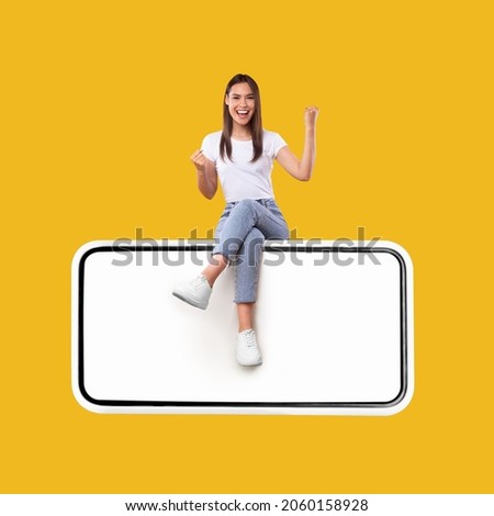 Yes. Excited Woman Sitting On Big Smartphone With Empty White Screen Shaking Clenched Fists, Cheerful Lady Celebrating Win Isolated On Yellow Orange Background, Mock Up Collage, Full Body Length Royalty-Free Stock Photo #2060158928