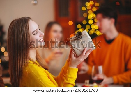 Young person giving wrapped gift to friend while sitting at table and celebrating Christmas together