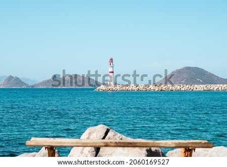 Lighthouse standing at the coast of Bodrum, Turkey. Red white lighthouse with islands on turquoise sea. Empty sitting bench.