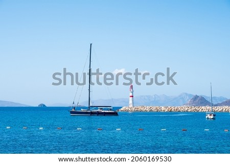 Lighthouse standing at the coast of Bodrum, Turkey. Red white lighthouse with islands and sailboats on turquoise sea.