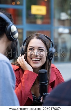 Young woman with microphone and headphones working outside conducting recording interview for tv or radio podcast. Female digital content creator working as a journalist 