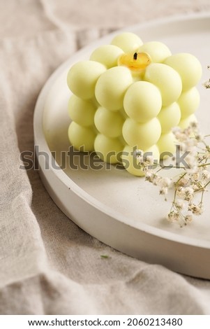 One white square bubble candle on a concrete tray on a linen table cloth with a mild focus on a blooming branch