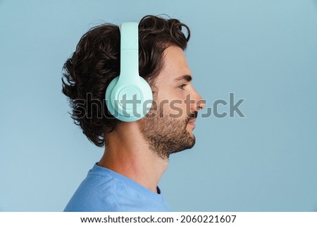 Young brunette man with bristle listening music with headphones isolated over blue background