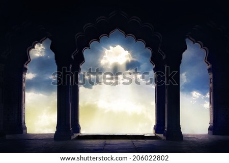 Indian arch silhouette in old temple at dramatic sunset sky with light hole in the clouds