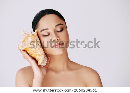 Pretty African American woman with closed eyes pressed conch seashell to her ear enjoy and dreams Royalty-Free Stock Photo #2060234561