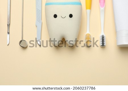 Tooth model with cute face, oral care products and dental tools on beige background, flat lay. Space for text