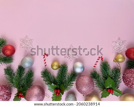 Christmas decorations, pine tree leaves, golden balls, snowflakes, red balls on pink background