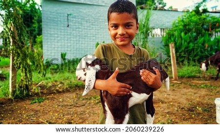 Young Indian boy holding the small goat with affection and smiling face.