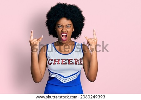 Young african american woman wearing cheerleader uniform shouting with crazy expression doing rock symbol with hands up. music star. heavy concept. 