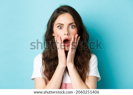 Oh my gosh. Close up portrait of shocked girl face, touching head and staring at camera startled, hear bad news, standing over blue background Royalty-Free Stock Photo #2060251406