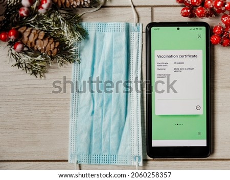 Phone with electronic Covid Vaccination Certificate and medical mask on Christmas background