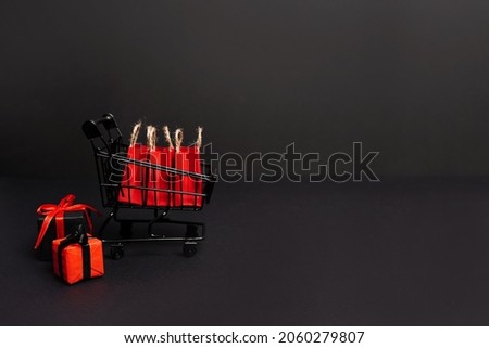 Black Friday sale shopping cart with red paper bags and gift boxes on black background