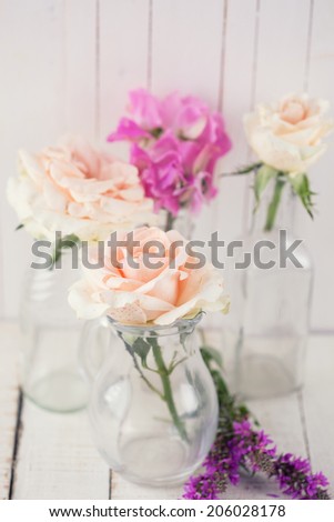 Fresh summer roses in glass bottles on white wooden background.