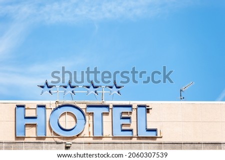Top view of a hotel, at noon, with a sign with the neon lights off that says "Hotel" and 4 stars above; behind a blue sky and to the right a television antenna.