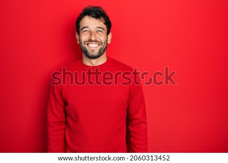 Handsome man with beard wearing casual red sweater with a happy and cool smile on face. lucky person. 