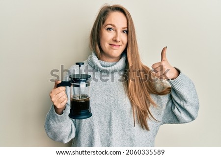 Young blonde woman drinking italian coffee smiling happy and positive, thumb up doing excellent and approval sign 