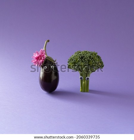 Girly look eggplant with pink autumn flower, and broccoli boy with eyes. Minimal creative funny couple concept on purple background.