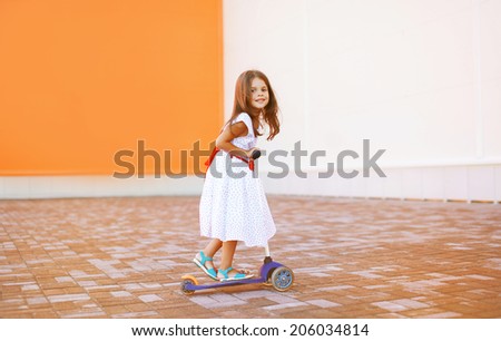Portrait of active little girl child skating on scooter in the city