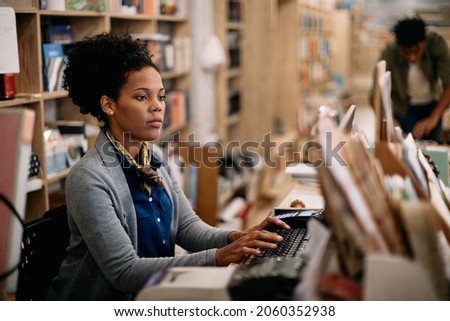 African American female librarian working on desktop PC at university library.  Royalty-Free Stock Photo #2060352938