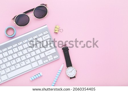 Computer keyboard with sunglasses and wrist watch on pink background