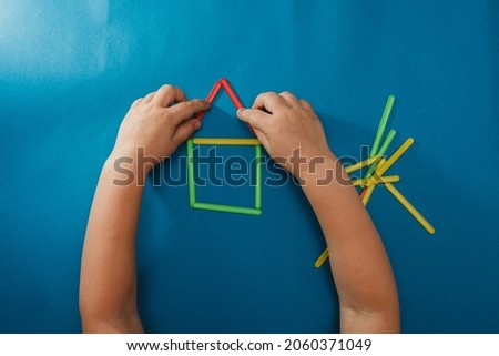 A small child assembled a house figurine. Children's hands with counting sticks isolated on a blue background.