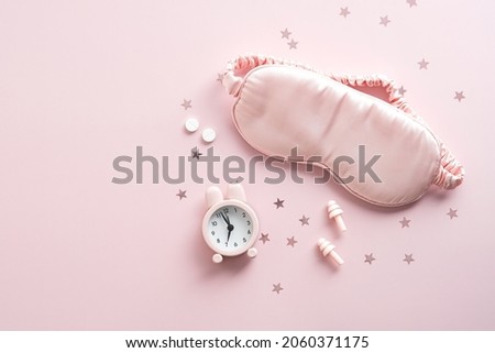Female eye mask, alarm clock, earplugs, pills on pink background with confetti. Insomnia treatment concept. Royalty-Free Stock Photo #2060371175