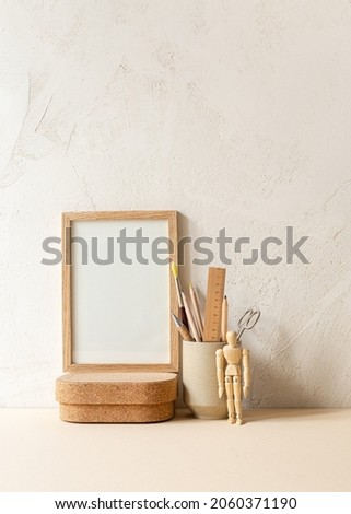 Blank wooden frame and, mug with arist tools against bright clay wall.
