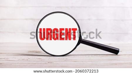 The magnifying glass stands vertically on a light background with the text URGENT