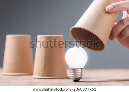 Closeup hand reveal where the light bulb is in three cups shell game, helpful tips, reveal the success idea concept, or FAQs